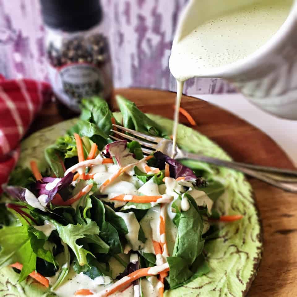 Oil-Free Vegan Ranch Dressing pouring on green salad on a green plate.