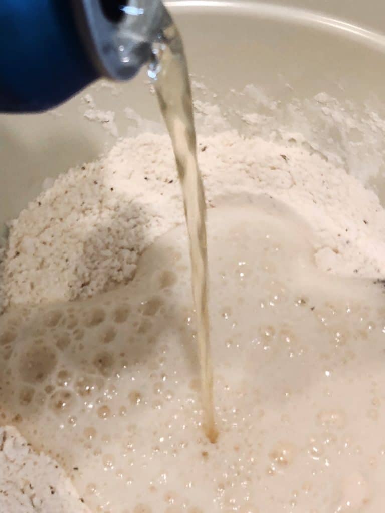 a stream of beer being poured in dry ingredients for garlic herb beer bread