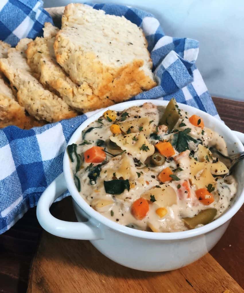 slices of garlic herb beer bread in basket with blue checkered napkin behind white bowl with creamy vegetable bow tie soup