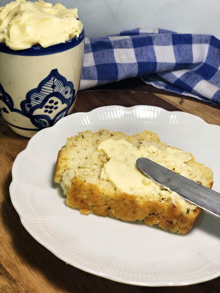 buttered garlic herb beer bread on white plate with crock of buttery spread and blue checkered cloth