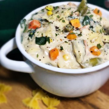 creamy vegetable pasta soup in white bowl with bow tie pasta in front