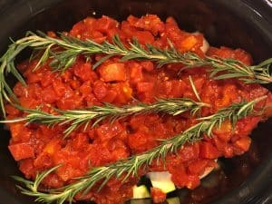three rosemary sprigs on top of diced tomatoes in the crockpot