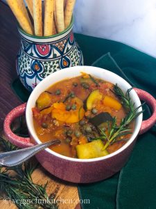 slow cooker butternut squash ratatouille in red bowl with green napkin and breadsticks