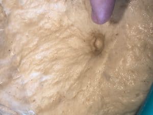 finger pushing dent into dough