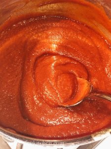 red bbq sauce in a pan stirred with a spoon