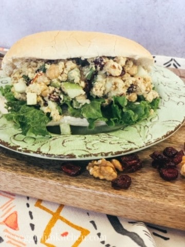 curried chickpea salad on bun on green plate on wooden tray
