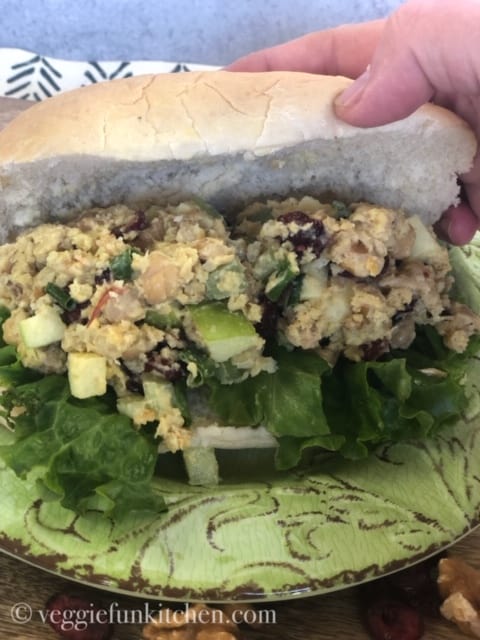 curried chickpea salad on bun being held in hands
