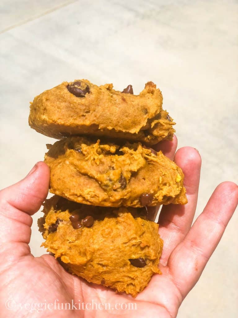 three pumpkin cookies with chocolate chips held in the hand