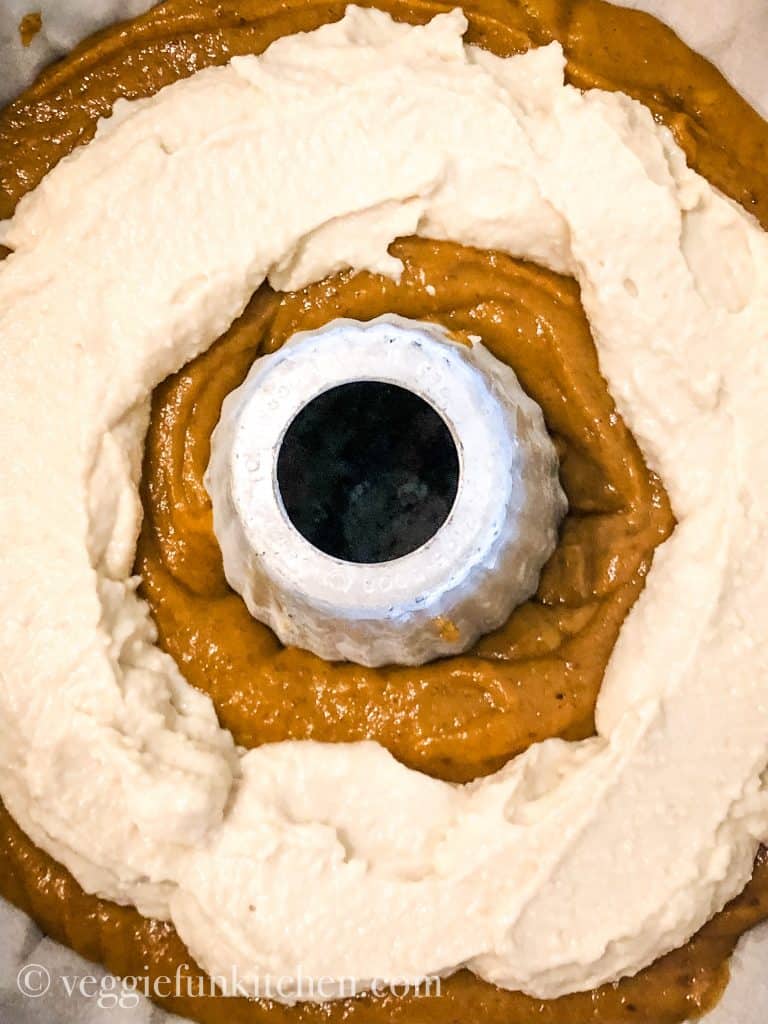 ring of vegan cream cheese placed on top of pumpkin cake batter in bundt pan