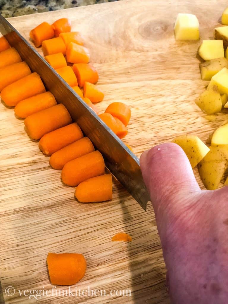 baby carrots lined up and being sliced with diced potatoes in the backgrond