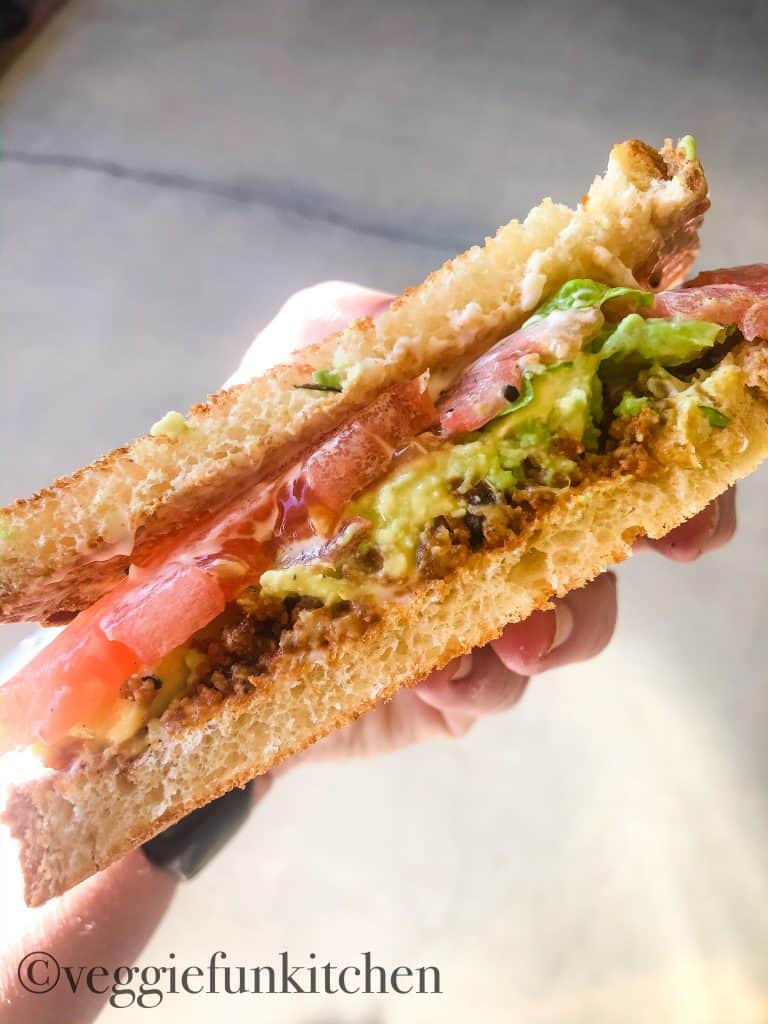 blt held in hand with tofu bacon crumbles as ingredient