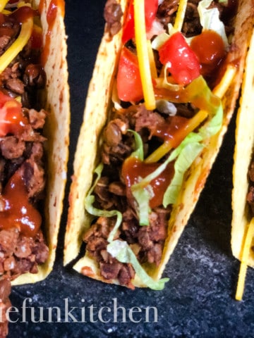 three tacos with vegan lentil taco meat on dark background