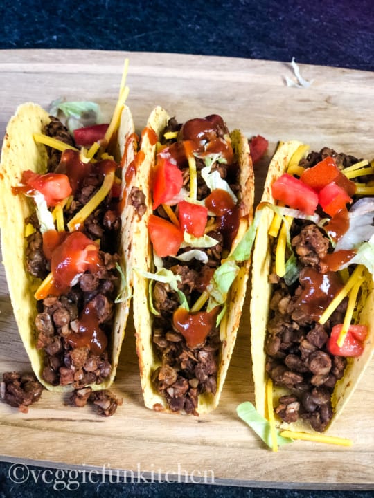 three tacos with vegan lentil taco meat on wooden board