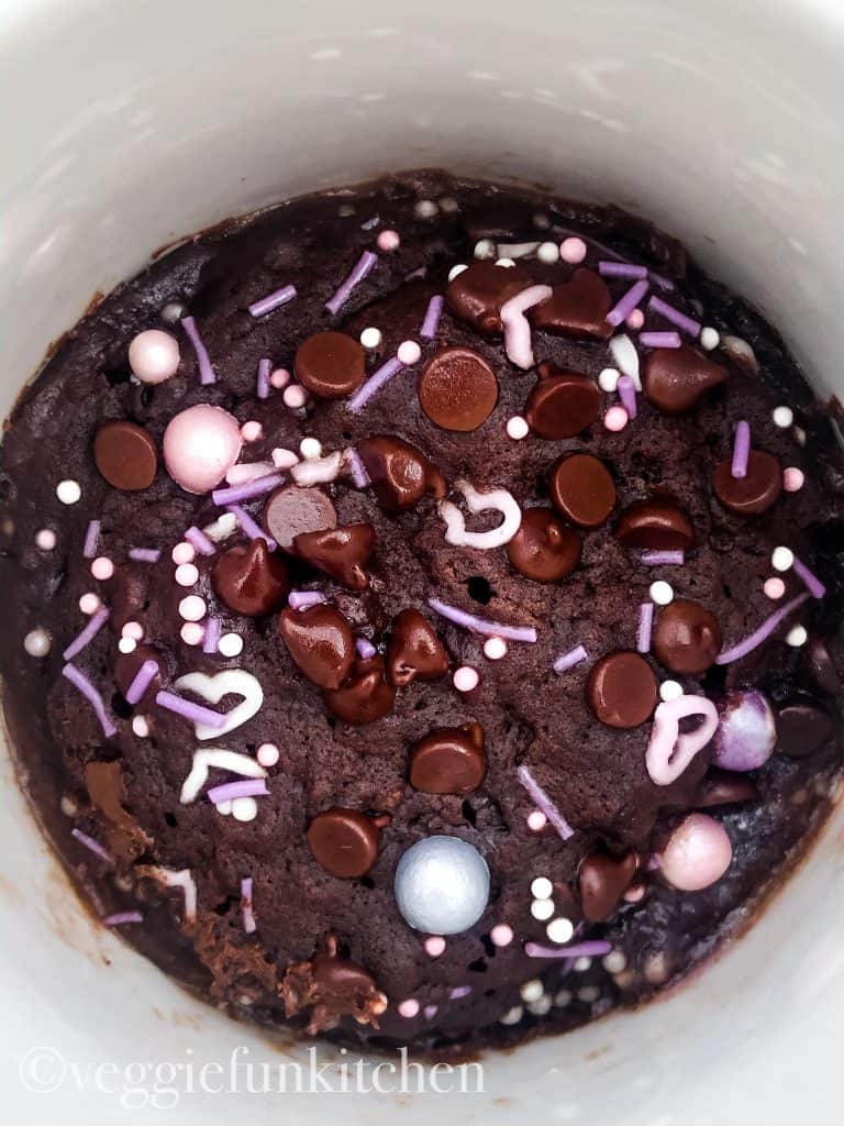 cooked vegan brownie in a mug with chocolate chips and pink and purple sprinkles on top.