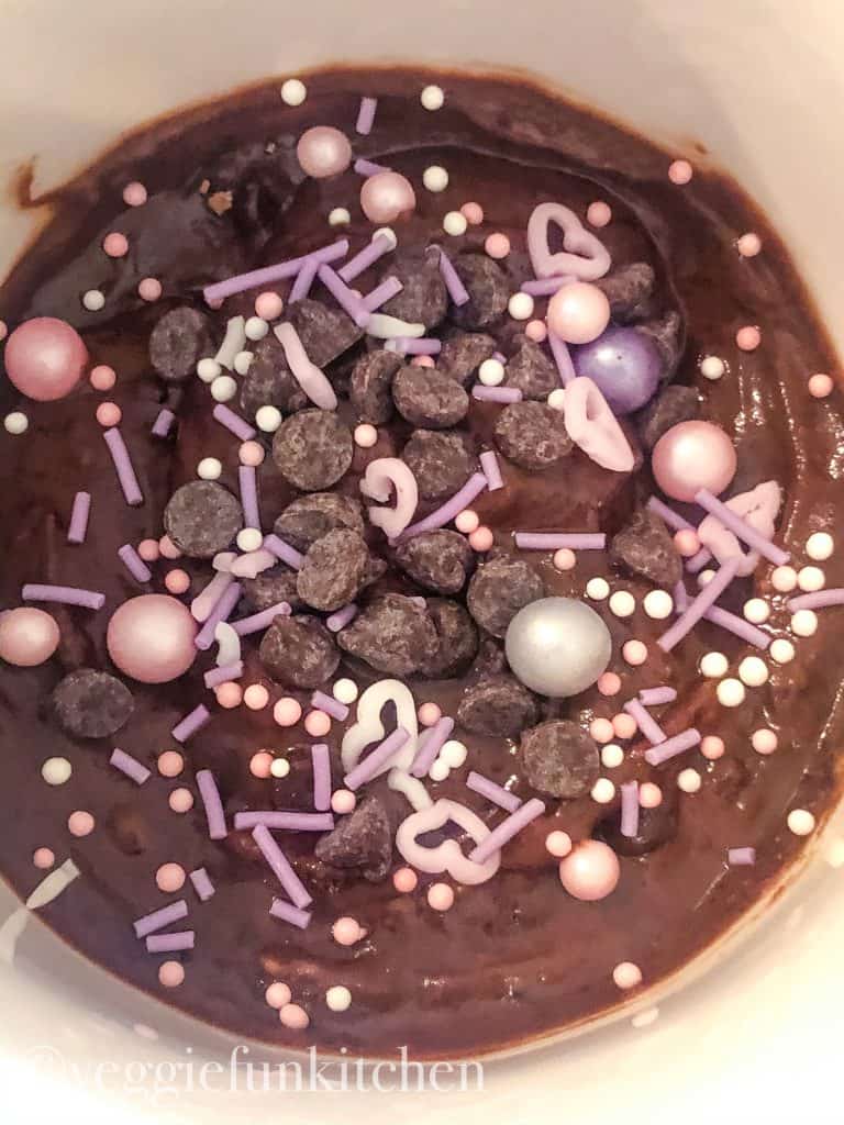 uncooked brownie in white mug with chocolate chips and pink and purple sprinkles on top