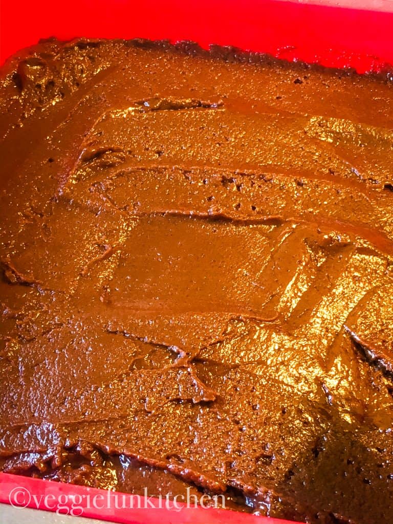 unbaked brownies in red pan with top smoothed