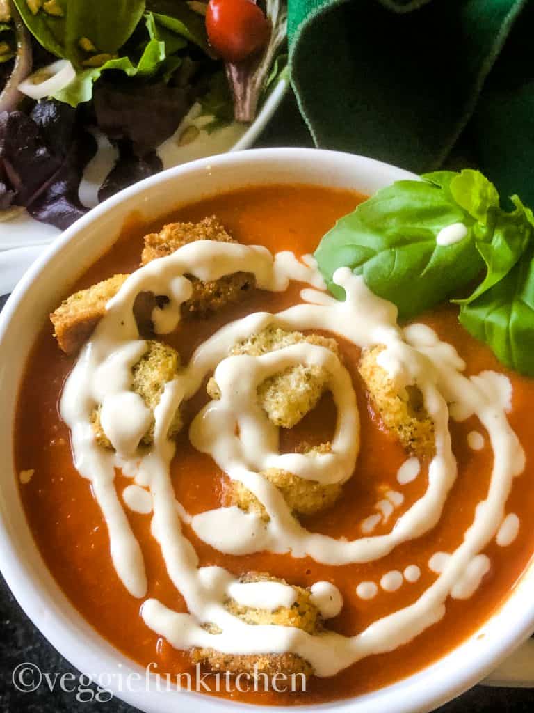 tomato soup with cashew cream drizzled on top with croutons and salad in background