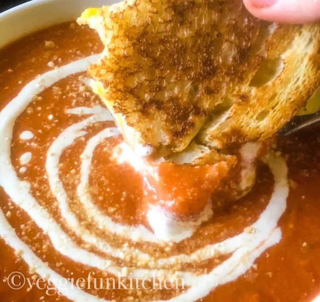 tomato soup with cashew cream drizzled on top with vegan grilled cheese dipped
