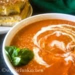 tomato soup with cashew cream drizzled on top with vegan grilled cheese in background