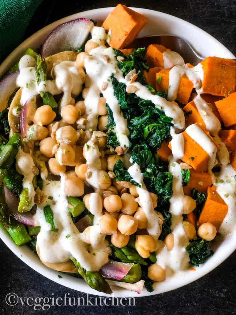 buddha bowl with asparagus, chickpeas, onioni, spinach, sweet potato all with a drizzle of garlic sauce