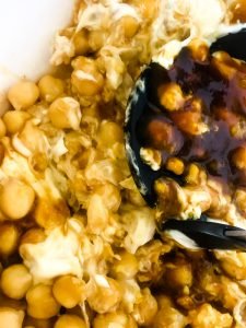 potato masher mashing chickpeas together with mayo and bbq sauce