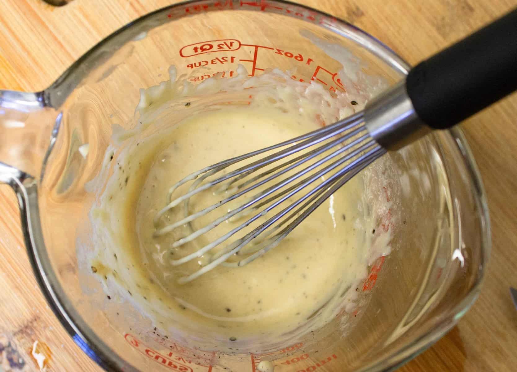 tahini dressing being whisked in glass measuring cup