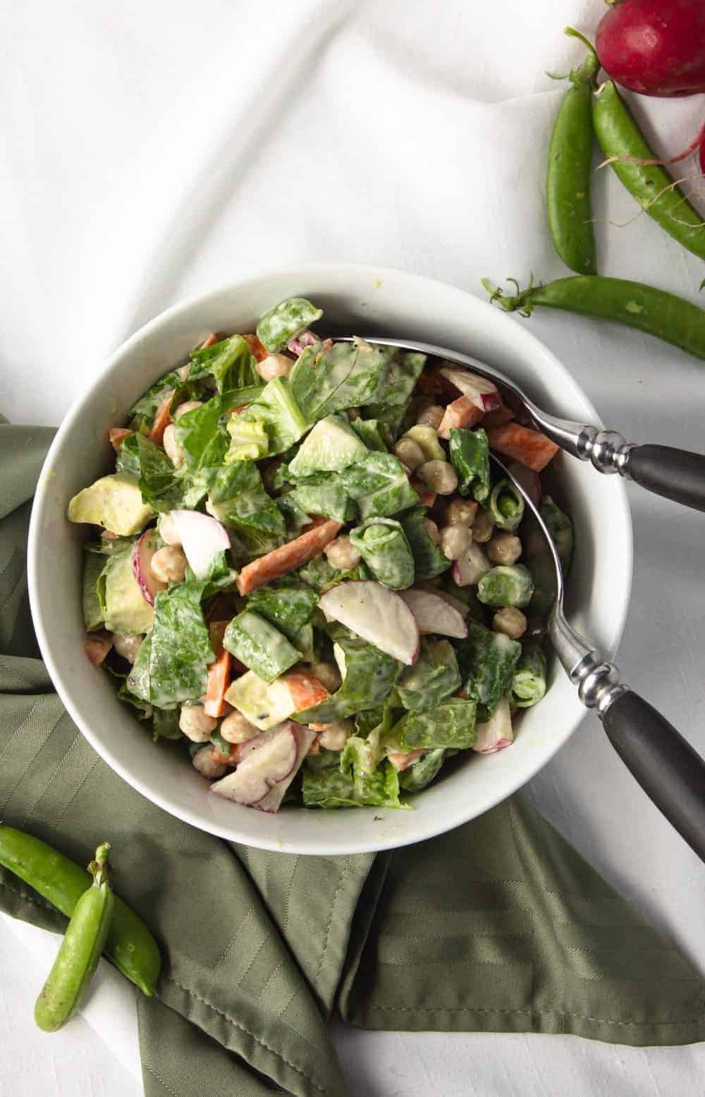 veggie salad in white bowl with green napkin and fork and spoon in bowl