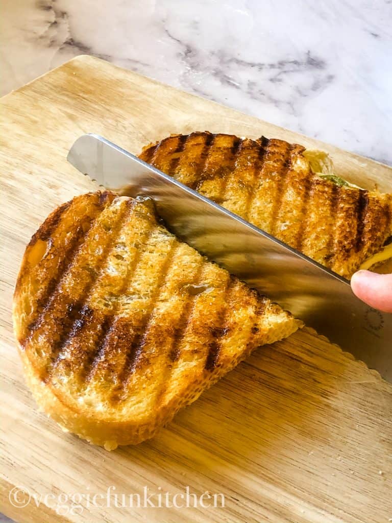 cooked panini sandwich on wooden cutting board being cut with knife
