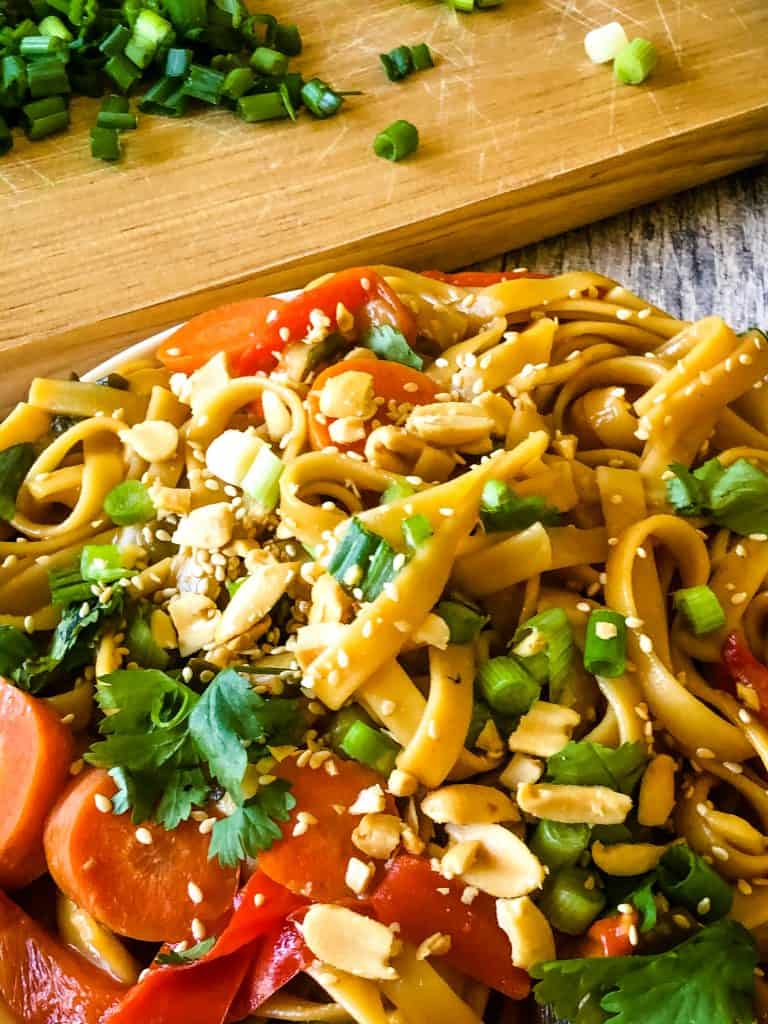 plate of peanut butter noodles with chopped green onions on wooden cutting board in background