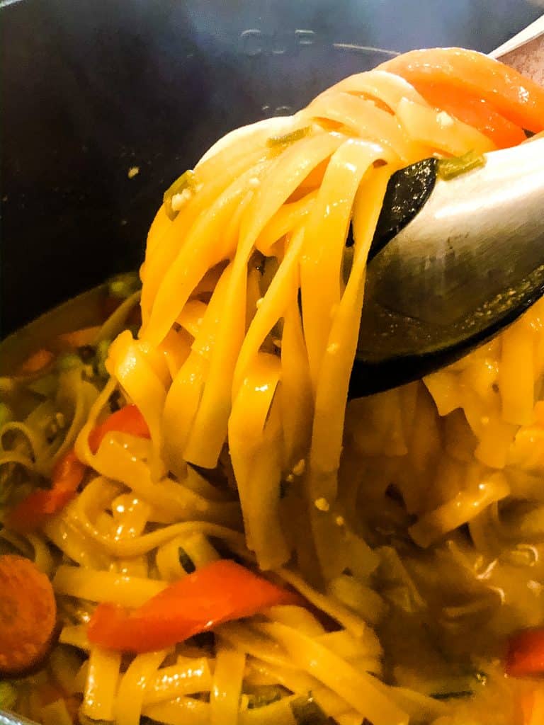 tongs stirring and lifting peanut butter noodles in Instant Pot