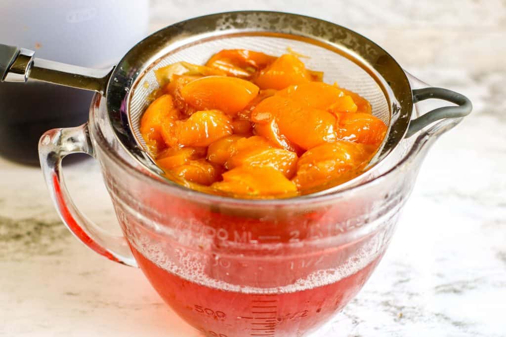 Peaches in simple syrup draining in a mesh strainer over a glass bowl