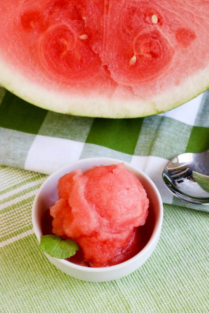 watermelon sorbet in white bowl with half watermelon and green checked cloth