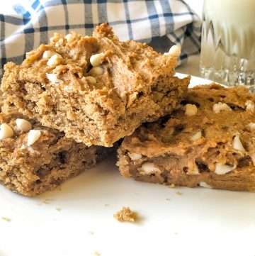 three blondies on plate with blue checked napkin and glass of oat milk in background