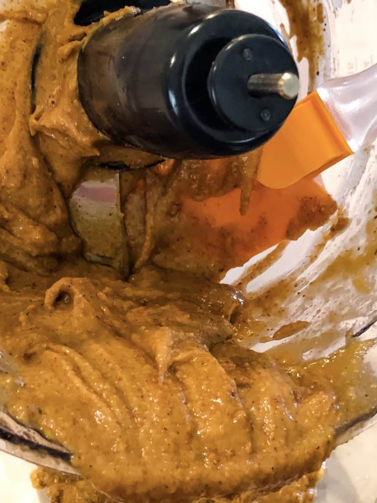 chickpea and almond butter mixture being scraped from food processor bowl with rubber spatula