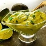 thick avocado sauce in glass gravy dish with limes and avocados in background