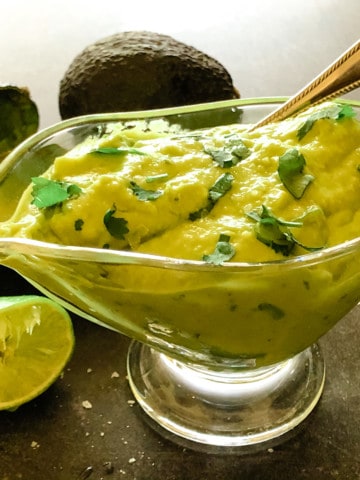 thick avocado sauce in glass gravy dish with limes and avocados in background