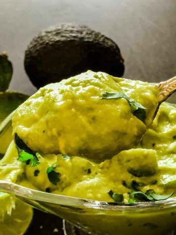 spooning out thick avocado sauce from glass dish with avocado halves in background