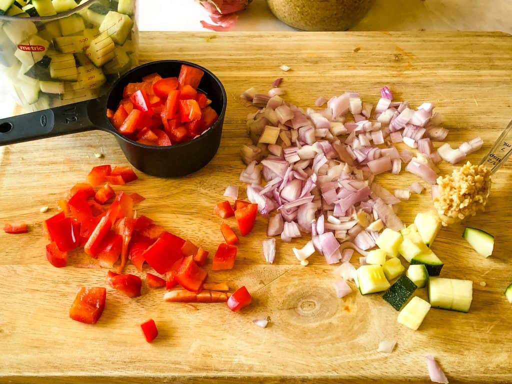 fresh ingredients needed for enchiladas including chopped zucchini, red bell peppers, and shallots