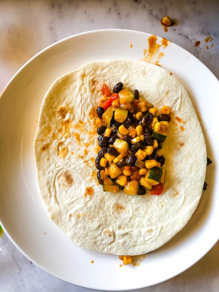 black beans and veggies on a tortilla ready to roll