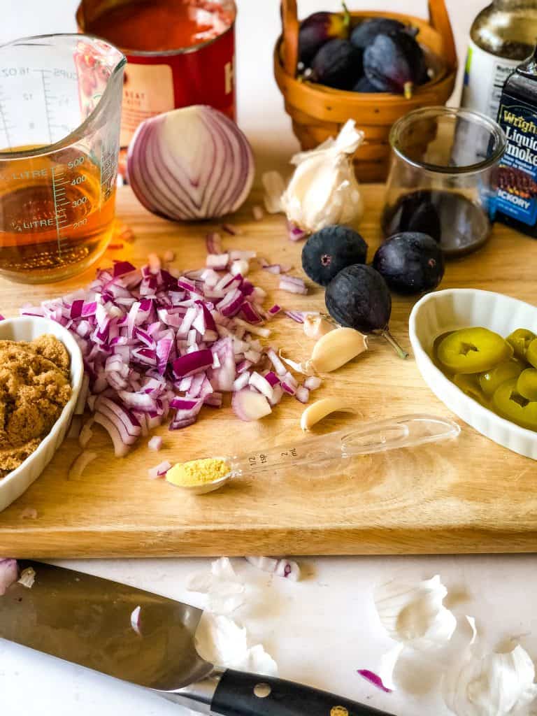 ingredients for bourbon bbq sauce including brown sugar, red onion, dried mustard, garlic, figs, jalapeno, worchershire sauce, liquid smoke, tomato sauce, and bourbon