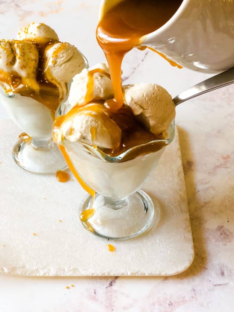 two glass ice cream dishes filled with sweet cream ice cream with caramel sauce being poured on top