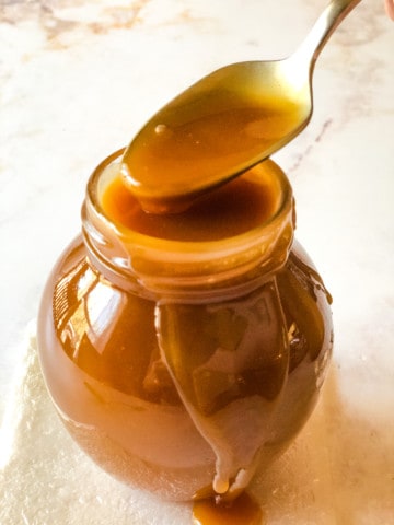 small jar of caramel sauce with spoon dipping in to scoop some out