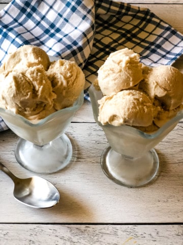 two glass ice cream dishes filled with sweet cream ice cream with blue plaid cloth in background