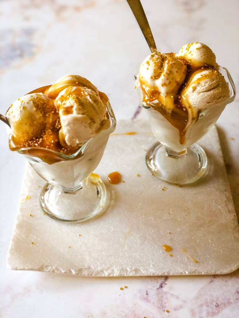 two glass ice cream dishes filled with sweet cream ice cream topped with caramel sauce and golden sprinkles