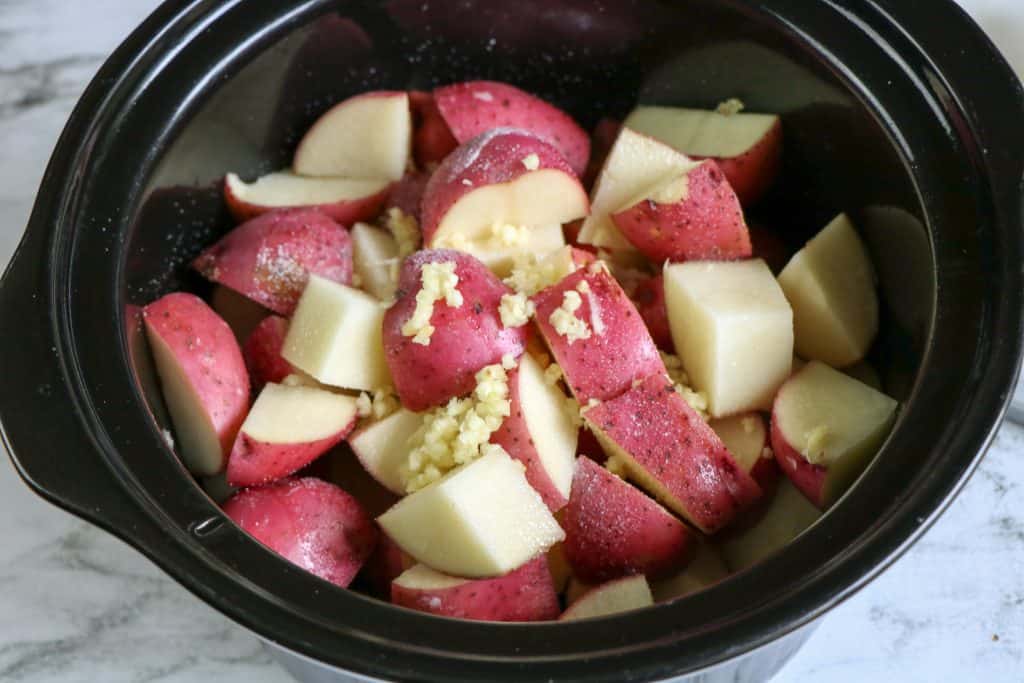 cut red potatoes and garlic in crockpot liner