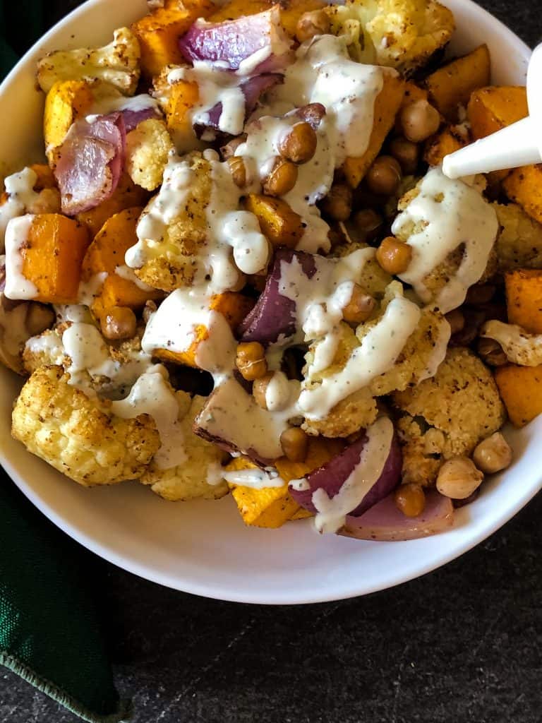 butternut squash and cauliflower roasted and in white bowl with jalapeno ranch squeezed on top