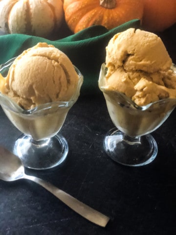 two glass ice cream dishes with pumpkin ice cream and pumpkins in background