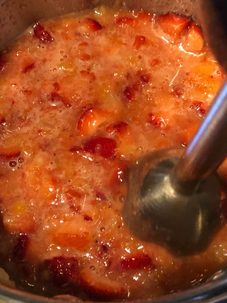 blending ingredients for strawberry topping before cooking using an immersion blender