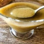a glass gravy boat containing vegan turkey gravy with a spoon dipping our a portions to show the many seaonings