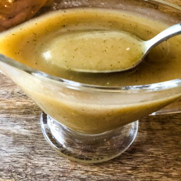 a glass gravy boat containing vegan turkey gravy with a spoon dipping our a portions to show the many seaonings